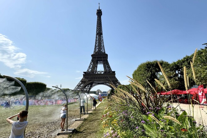 Paris, France - July 30, 2024 - Children and adults cooling down under Arch Mist Poles on the Champs de Mars outside the Eiffel Tower Stadium in a heatwave during the Summer Olympics in Paris, France