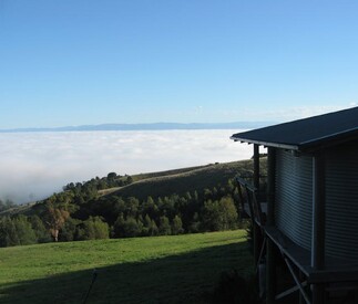 fog in the valley below and blue skies and green grass and trees at the cottage level