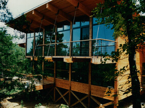 Modern heavy timber post and beam house with cedar siding. View of south facing window wall with suspended decks and large overhanging eave.