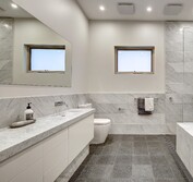 Interior view of large bathroom with marble vanity, toilet, undermount bathtub and open shower. Main Bath with honed Carrara marble wall tiles and vanity with cut in sink. Honed black granite floor tiles.