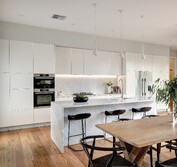 Interior view showing close up of kitchen island with honed Carrara benchtop, wood flooring and whie painted cabinet doors, LED cabinet lighting in kitchen.