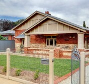 View from front yard of red brick bungalow with cream and tan paint. Restored bungalow featuring new window canopy, restored sandstone, corrugated metal roof, period fencing, period lighting and new paint scheme.