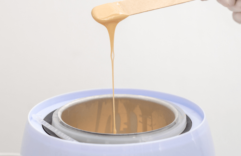 Image of wax dripping from stick above hot pot of wax
