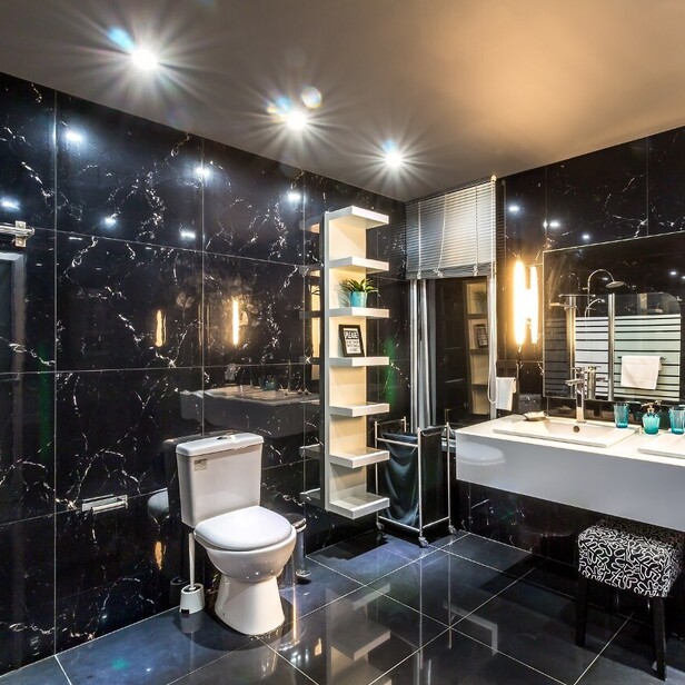 a photo of a very bright bathroom, multiple shiny surfaces including mirrors, tiles, basin, lighting.